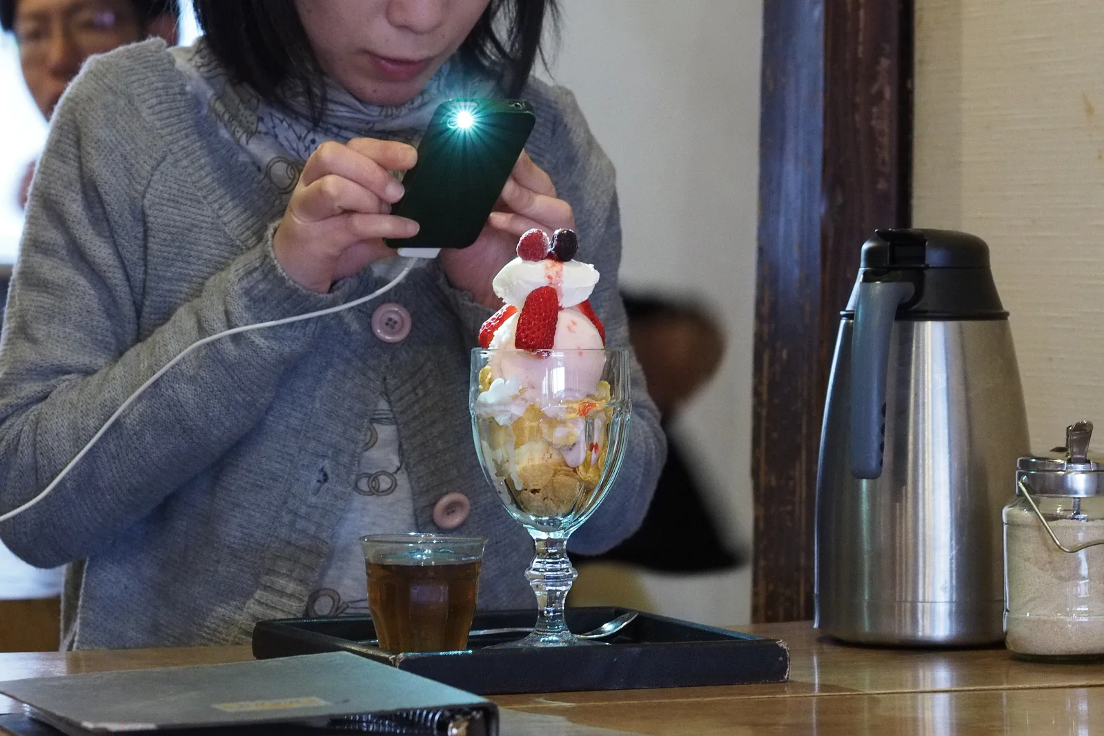 Una mujer en una cafetería hace una foto con flash a una copa de helado con fresas antes de comérsela